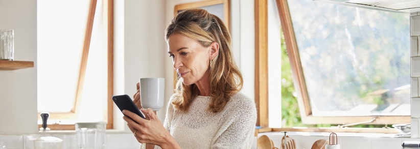 standing woman reading her phone while drinking coffee in kitchen