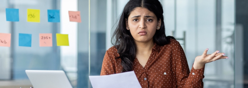 Confused business woman looking at paper and computer