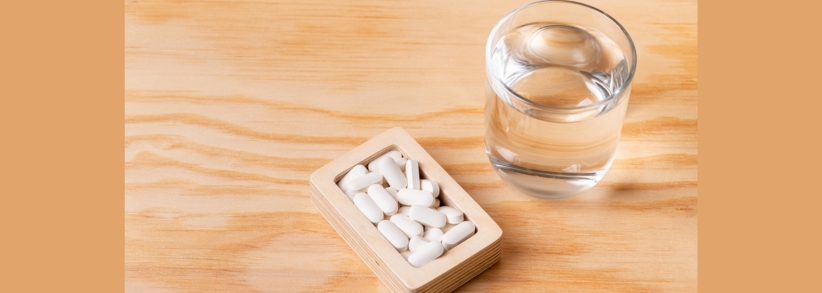 Pill box with nutraceuticals and glass of water on wooden table